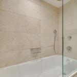 Bad mit Dusche und Badewanne, belegt mit Steinplatten und Glaswand.