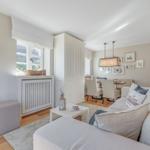 Wohn- und Essbereich mit Sofa, Tisch und Stühlen. Fenster und Wanddekoration sichtbar.