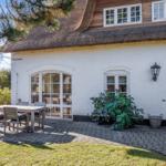 Weiße Hauswand mit blauer Tür und strohgedecktem Dach. Außenterrasse mit Tisch und Stühlen.