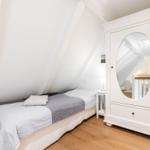 Schlafzimmer mit Dachschräge, weißem Schrank mit Spiegel und Bett mit grauem und weißem Bettzeug.