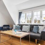 Wohnzimmer mit Sofa, Couchtisch und Fenstern. Holzboden und weiße Wände.