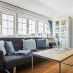 Ein Wohnzimmer mit Sofa, Tisch und Fenstern.