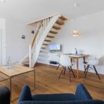 Wohn- und Essbereich mit Holzboden, Treppe und weißer Einbauküche.