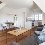Wohnbereich mit Sofa, Esstisch, Küche und TV unter Dachschrägen.