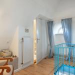 Schlafzimmer mit Holzboden, blauer Babygitter, Bücher und Tür zur Dusche.