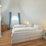 Schlafzimmer mit weißem Bett, Holzboden und Schrank. Fenster mit blauen Vorhängen.