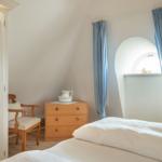 Schlafzimmer mit Bett, Schrank und Stuhl. Fenster mit blauen Vorhängen.