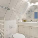 Badezimmer mit Duschbereich, Waschbecken und Toilette unter schräger Decke.