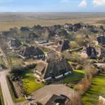 Dorf mit strohgedeckten Häusern und grünen Wiesen unter blauem Himmel.