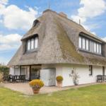 Haus mit strohgedecktem Dach und weißer Fassade. Außenbereich mit Tisch, Stühlen und Pflanzen.