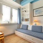 Zimmer mit Fenster, Bücherregal und Sitzbank mit blauen Kissen.