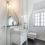 Bathroom with shower, sink, and toilet. Window with grid.