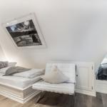 Room with two beds, white chair, and wall art under sloped ceiling.
