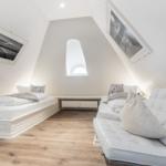 Room with two beds and sofa under sloped ceilings. Wooden floor and window.