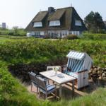 Terrasse mit Strandkorb und Tisch. Hintergrund: traditionelle Strohdachhäuser.