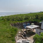 Terrasse mit Tisch und Stühlen, Blick auf das Meer und grüne Wiesen.