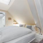 Schlafzimmer mit Dachschrägen, Bett, Nachttisch und Sessel. Durchgang zur Dusche.