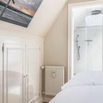 Schlafzimmer mit Dachschrägen, weißer Einbauschränke und Blick in Dusche.