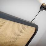 Black wall lamp next to a bed with woven headboard.