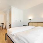 Bedroom with double bed, white walls, and wooden floor. Two wall lamps are mounted.