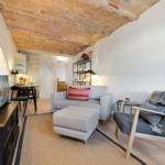 Living room with sofa, armchair, and brick ceiling. Kitchen in the background.