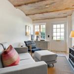 Living room with sofa, armchair, and TV under wooden beam ceiling.