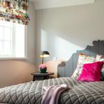 Schlafzimmer mit Bett, Nachttisch und Fenster mit Vorhang.