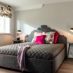 Schlafzimmer mit Bett, Nachttischen und Fenster mit Vorhang.