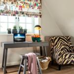 Schreibtisch mit Laptop, Stuhl und Zebra-Stuhl unter Fenster mit Pflanzen.
