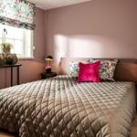 Schlafzimmer mit Bett, Kissen, Nachttischen und Fenster mit Blumenrollo.