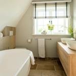 Bad mit Badewanne, Doppelwaschbecken und Fenster mit Blumen.