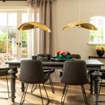 Esszimmer mit Tisch, Stühlen und goldenen Deckenleuchten. Fenster mit Blick auf Garten.