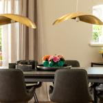 Esstisch mit Stühlen, goldenen Lampen und Blumenarrangement