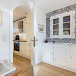 Küche mit weißer Einbauküche und Holzboden. Wand mit blau-weißen Fliesen und Schrank.