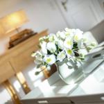 Weißer Blumenstrauß in Vase auf Tisch neben Wasserflasche und Glas.