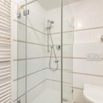 Bad mit Dusche, Toilette und Heizung. Fliesen mit beige Streifen.