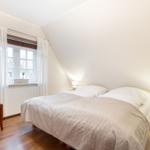 Schlafzimmer mit Dachbodenfenster, Bett, Nachttisch und Holzstuhl.