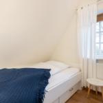 Schlafzimmer mit Dachschräge, Bett mit blauer Decke und Fenster mit Vorhängen.