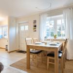 Esszimmer mit Holztisch, Stühlen und Fenster. Küche im Hintergrund.