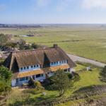 Haus mit Strohdach und Garten. Blick auf grüne Landschaft und Straße.