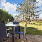 Terrasse mit Tisch und Stühlen, Grasfläche und Bäume im Hintergrund.