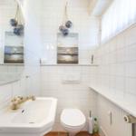 Badezimmer mit Waschbecken, Toilette und Spiegel an weißen Fliesenwänden.