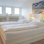 Schlafzimmer mit weißem Bett, zwei Nachttischen und Fenstern mit Blick nach draußen.