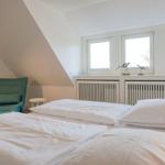 Schlafzimmer mit Doppelbett, grüner Sessel und Fenstern.