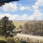 Blick aus dem Fenster auf Felder, Bäume und einen blauen Himmel mit Wolken.