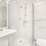 Badezimmer mit Dusche, Waschbecken und Toilette. Weiße Fliesen und goldene Armaturen.