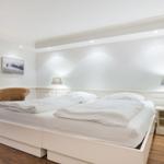 Schlafzimmer mit weißem Bett, Nachttisch und Lampe. Wandbilder und Holzboden.