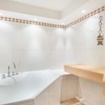 Badezimmer mit Badewanne, Holzbank und Wandfliesen mit Muster.