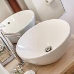 White vessel sink on wooden vanity with modern faucet.