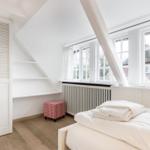 Bedroom with sloped ceiling, windows, and white bed.